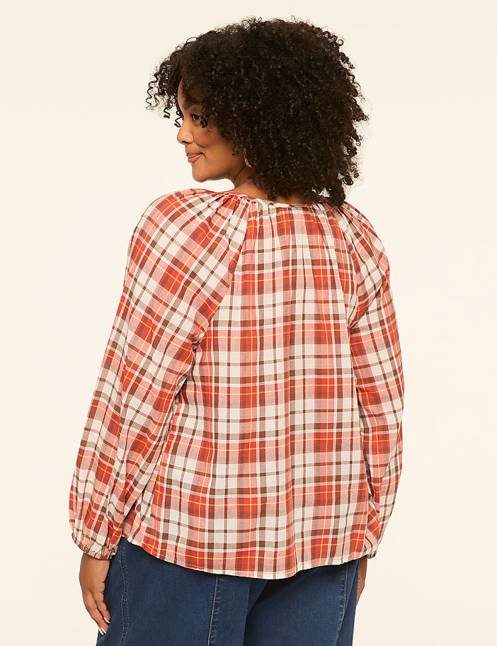 A woman in a plaid shirt stands against a plain, light-colored background.