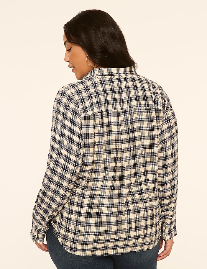 A woman in a blue and white plaid shirt stands against a plain, light-colored background.