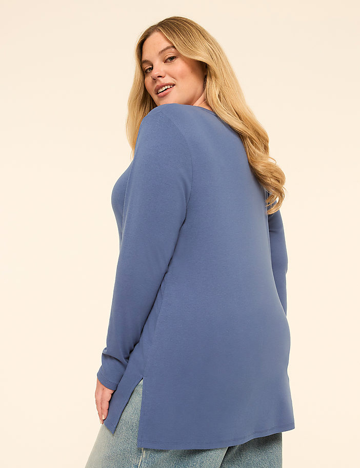 A woman in a blue tunic and jeans poses against a plain, light-colored background.