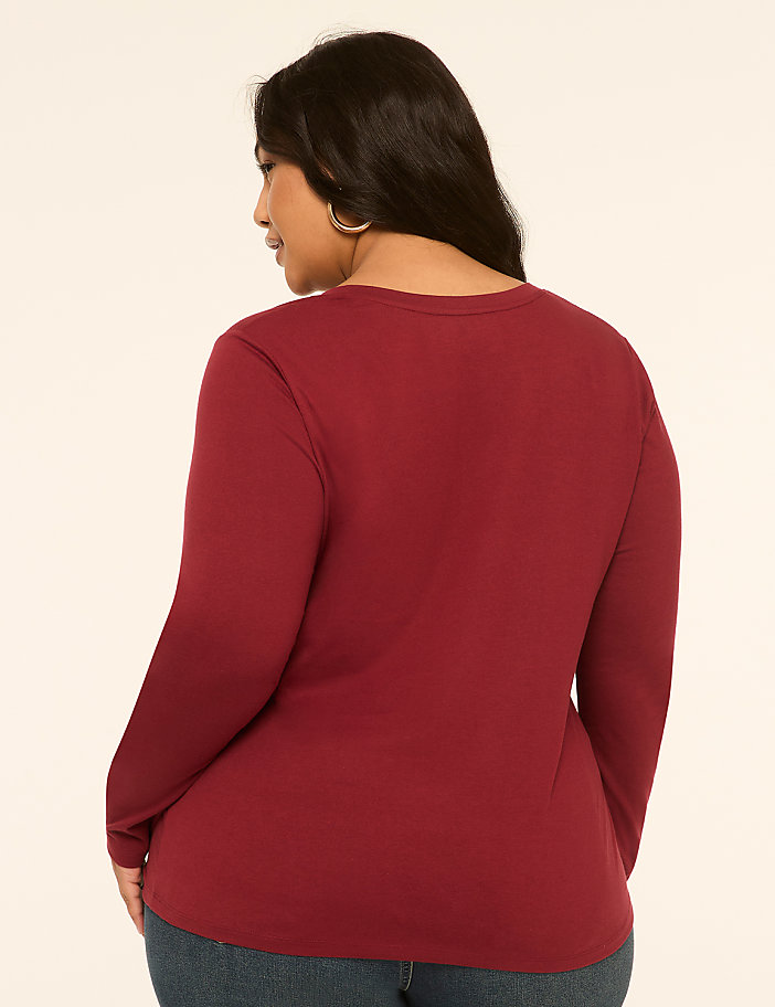 A woman in a maroon long-sleeved shirt stands against a plain, light-colored background.