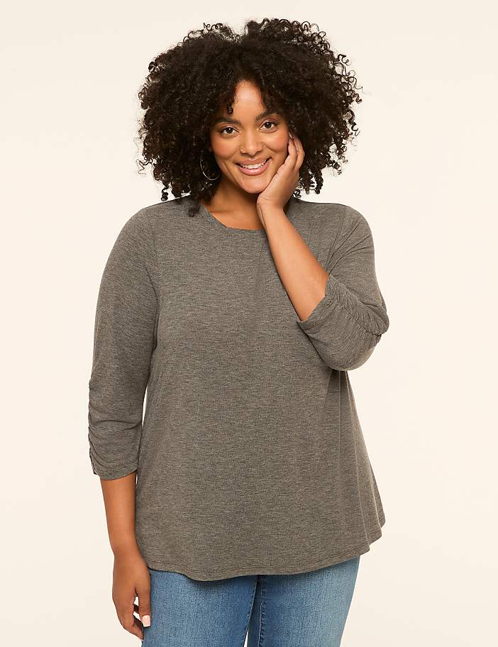 A smiling woman with curly dark hair and a grey shirt poses against a plain cream background.