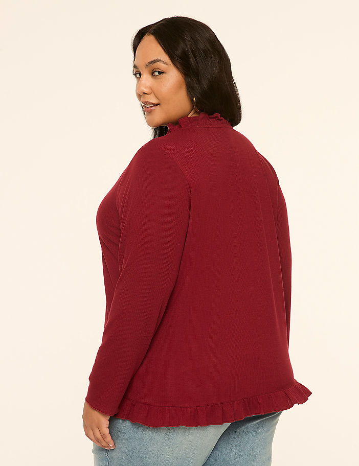 A woman in a maroon ruffled top and jeans stands against a plain, light-colored background.