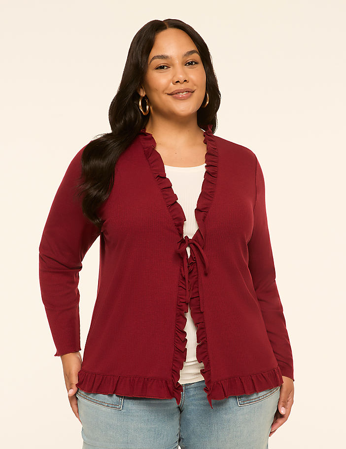 A woman in a maroon ruffled cardigan stands against a plain, light-colored background.