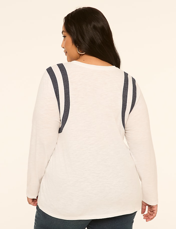 A woman in a white long-sleeved shirt with navy stripes on the shoulders stands against a plain, light-colored background.