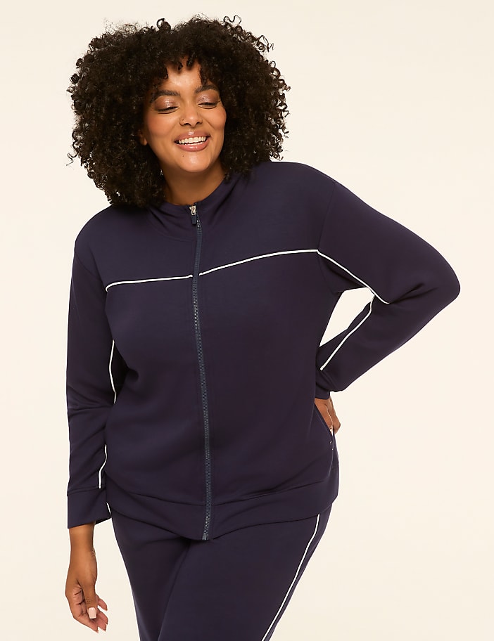 A smiling woman in a navy blue tracksuit with white piping stands against a plain, light-colored background.