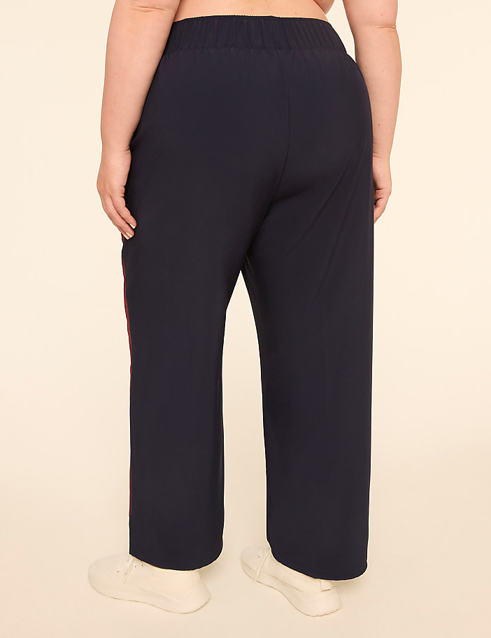A person wearing dark blue pants with a red stripe down the side stands against a plain, light-colored background.