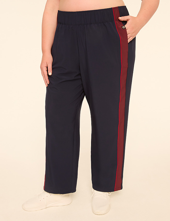 A person wearing navy blue track pants with a maroon stripe stands against a plain, light-colored background.