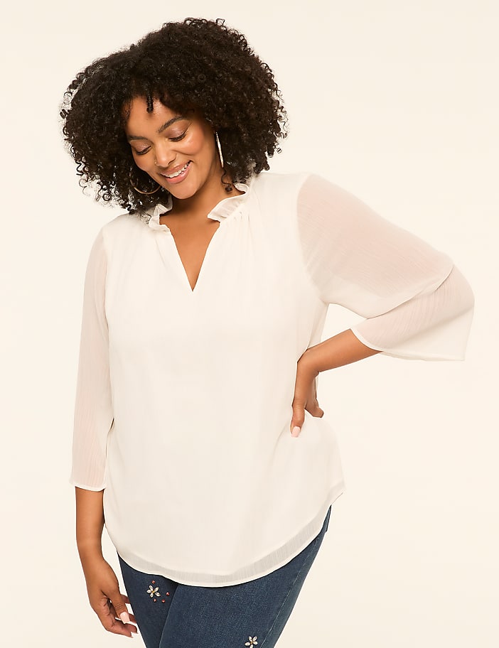 A smiling woman in a white blouse stands against a plain, light-colored background.