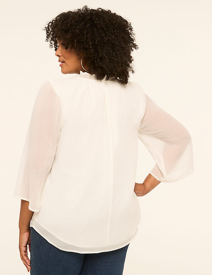 A woman in a white blouse stands against a plain, light-colored background.