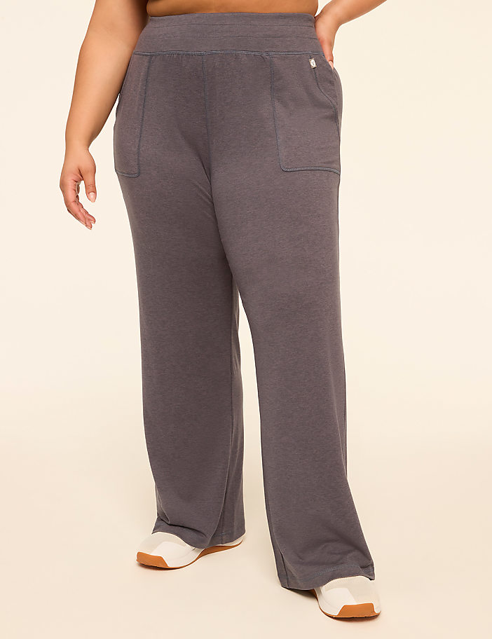 A person wearing dark gray wide-leg sweatpants with white sneakers stands against a plain, light-colored background.