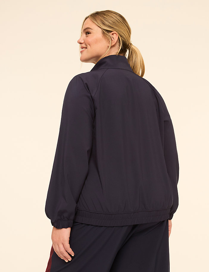 A woman in a navy jacket and pants stands against a plain, light-colored background.