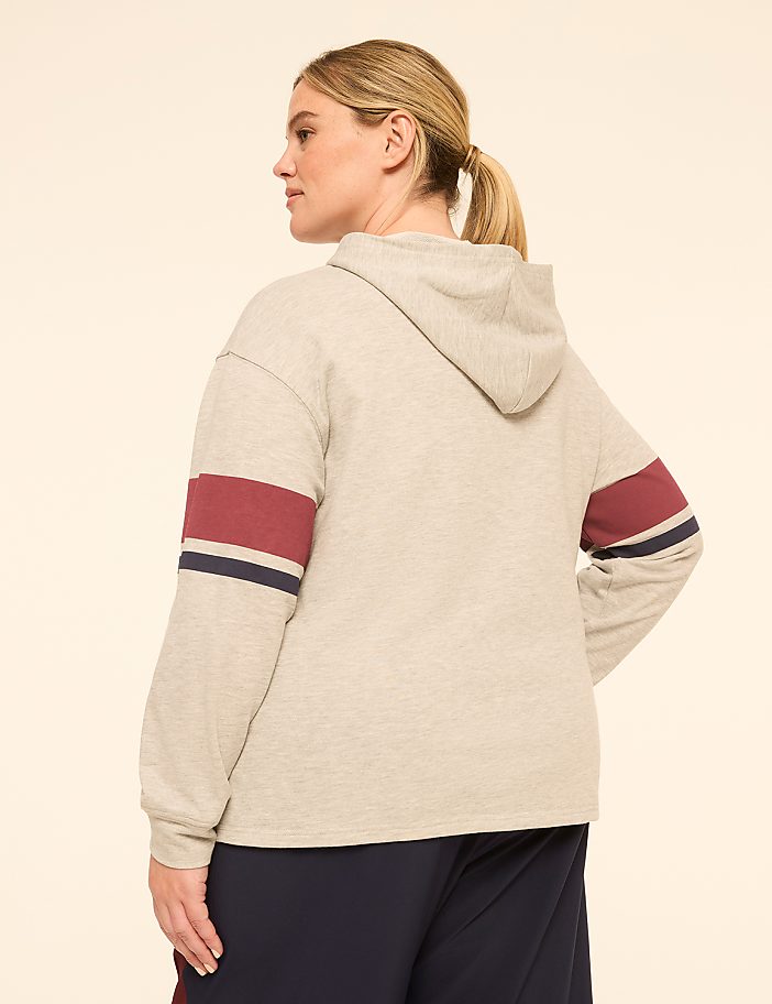 A woman in a grey hoodie with striped sleeves stands against a plain, light-colored background.