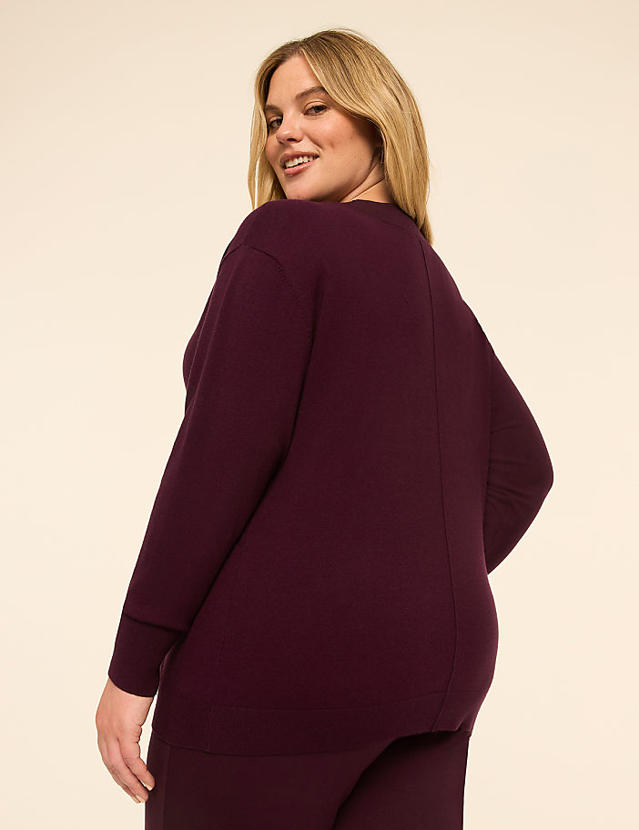 A woman in a burgundy sweater and pants stands against a plain, light-colored background.