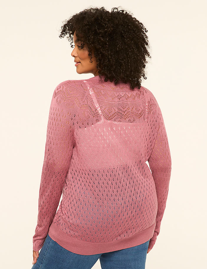 A woman in a pink open-knit cardigan stands against a plain, light-colored background.