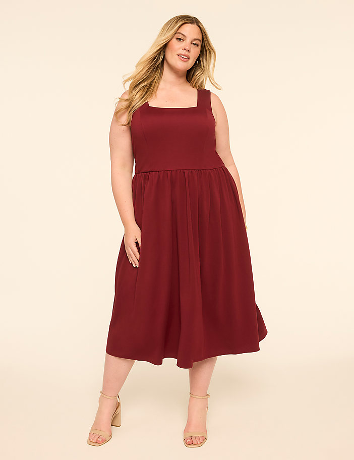 A woman in a maroon dress stands against a plain, light-colored background.