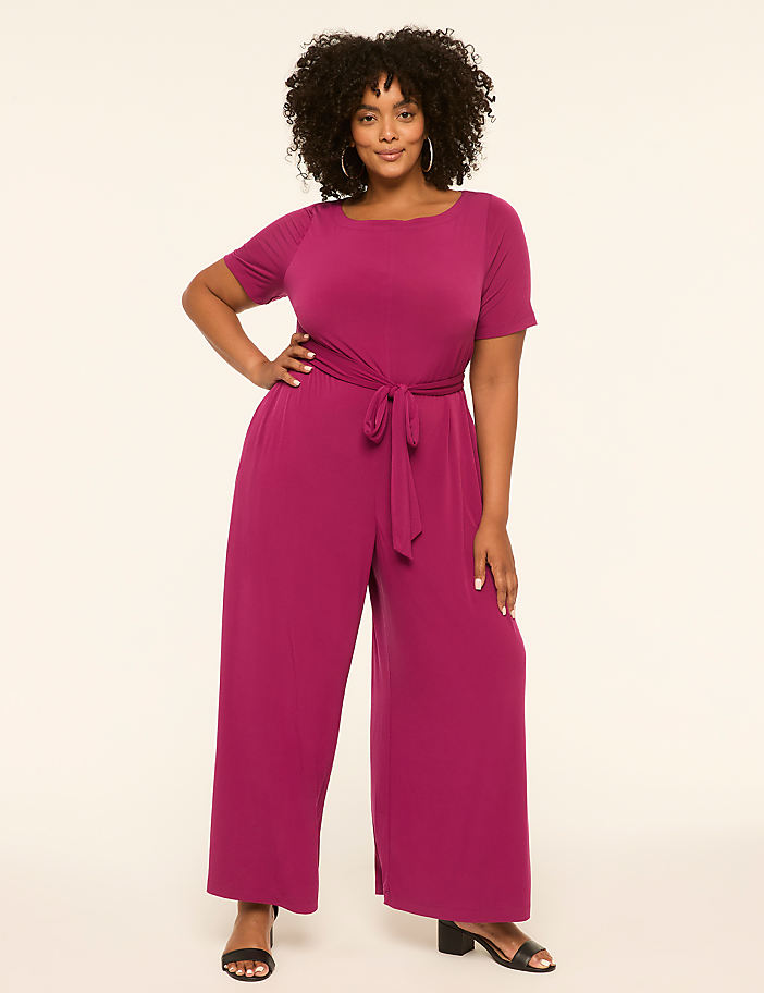 A woman in a magenta jumpsuit stands against a plain, light-colored background.