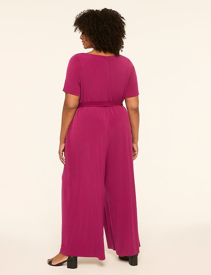 A woman in a magenta jumpsuit stands against a plain, light-colored background.