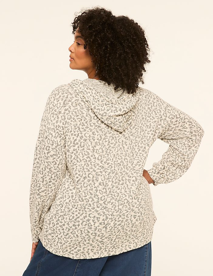 A woman in a leopard-print hoodie stands against a plain, light-colored background.
