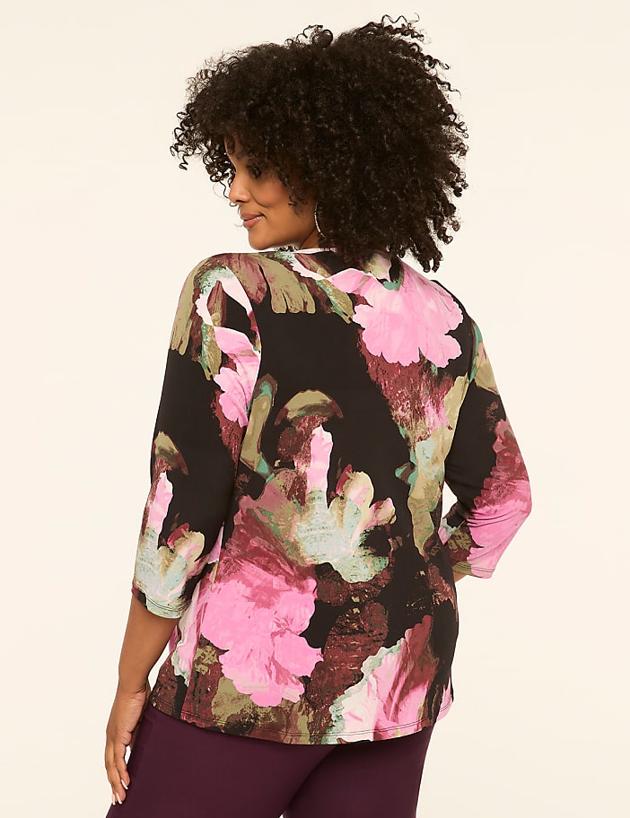 A woman in a floral blouse stands against a plain, light-colored background.