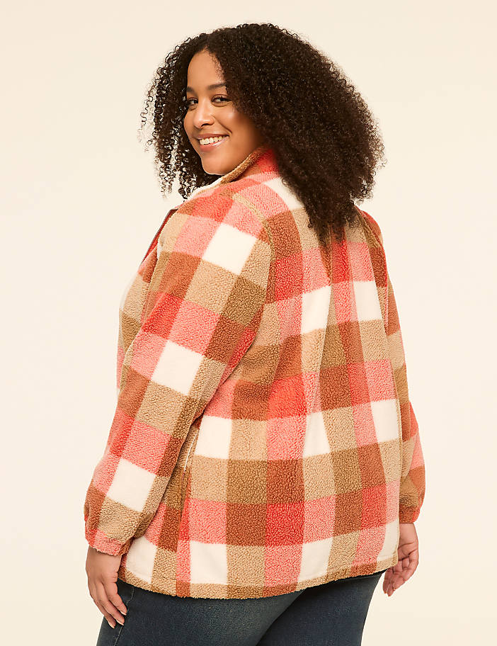 A woman with curly hair smiles over her shoulder, wearing a fuzzy plaid jacket in the foreground against a plain, light-colored background.