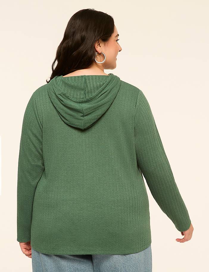 A woman in a green hooded sweatshirt stands against a plain, light-colored background.