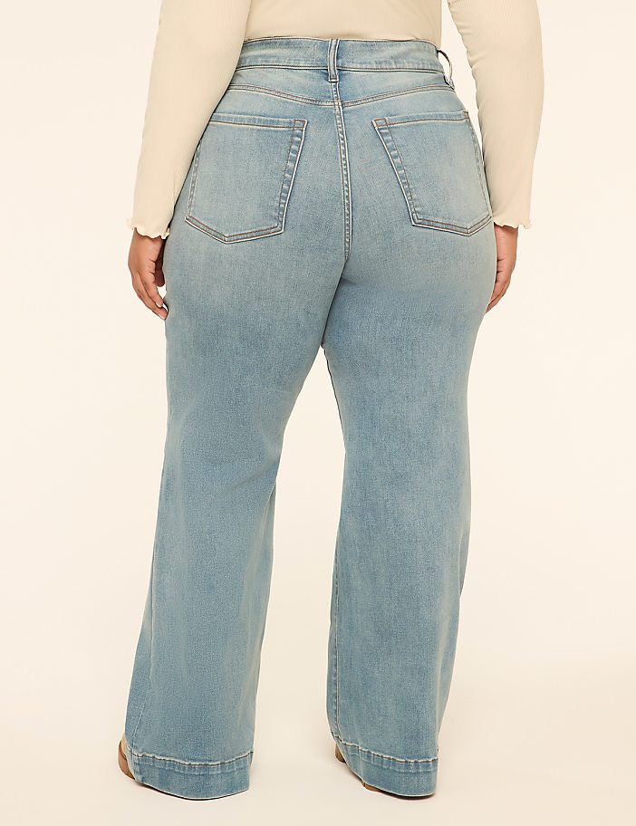 A person wearing light wash wide-leg jeans stands against a plain, light-colored background.
