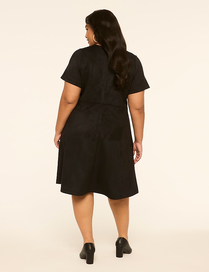 A woman in a black dress stands against a plain, light-colored background.
