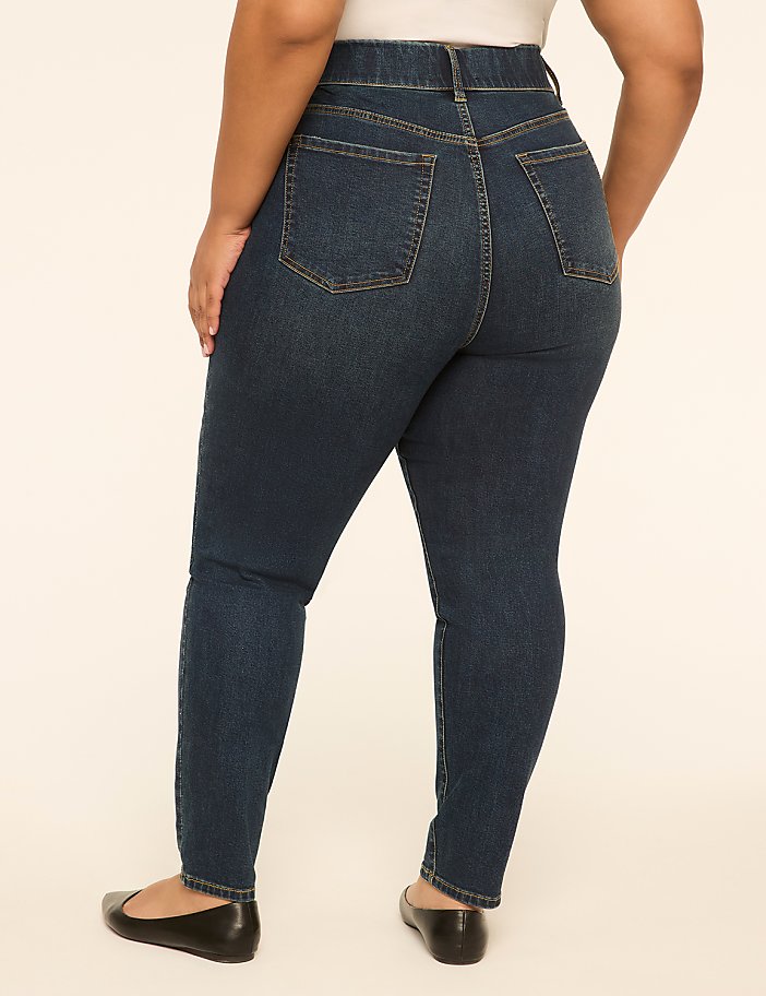A person wearing dark wash skinny jeans and black ballet flats stands against a plain, light-colored background.