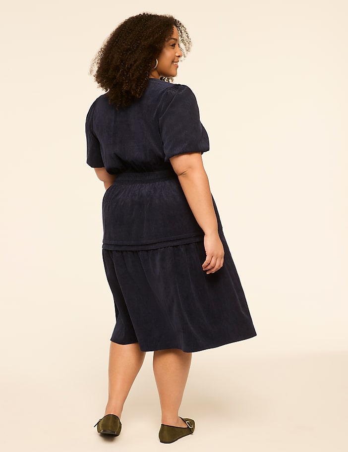 A woman in a navy blue dress stands against a plain, light-colored background.