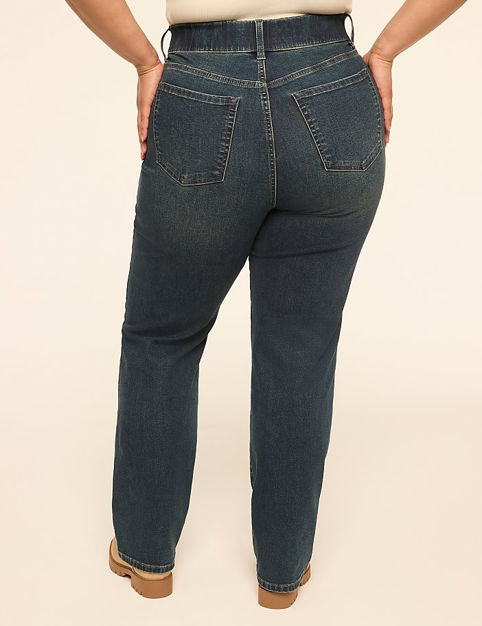 A person wearing dark wash denim jeans stands with their hands on their hips against a plain, light-colored background.
