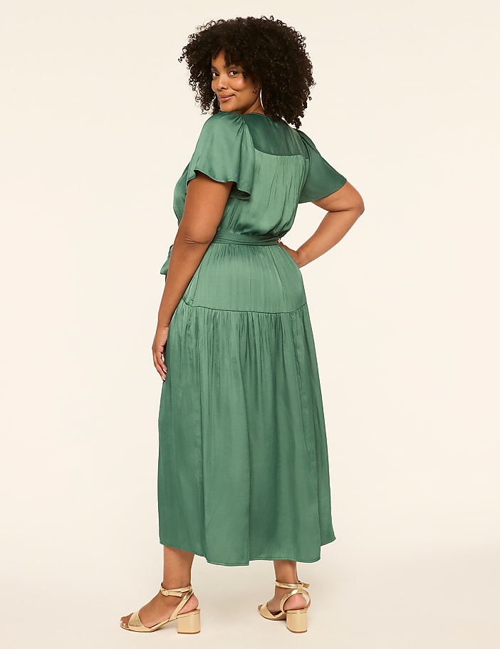 A woman in a green dress stands against a plain, light-colored background.