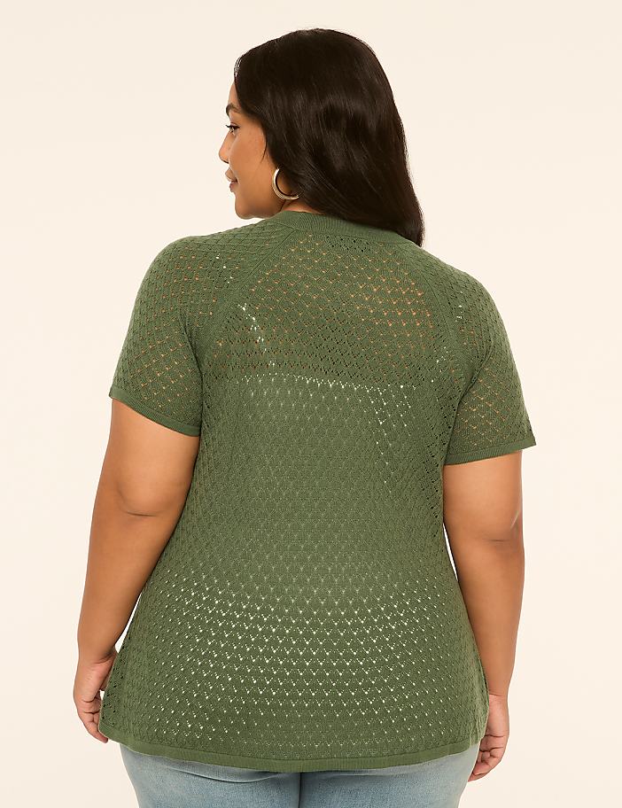 A woman in a green, short-sleeved, open-knit cardigan stands against a plain, light-colored background.