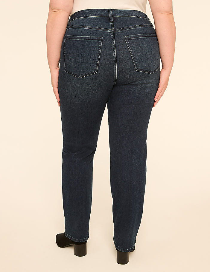 A person wearing dark wash denim jeans and black heels stands against a plain, light-colored background.
