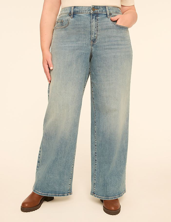 A person wearing light-wash wide-leg jeans and brown boots stands against a plain, light-colored background.