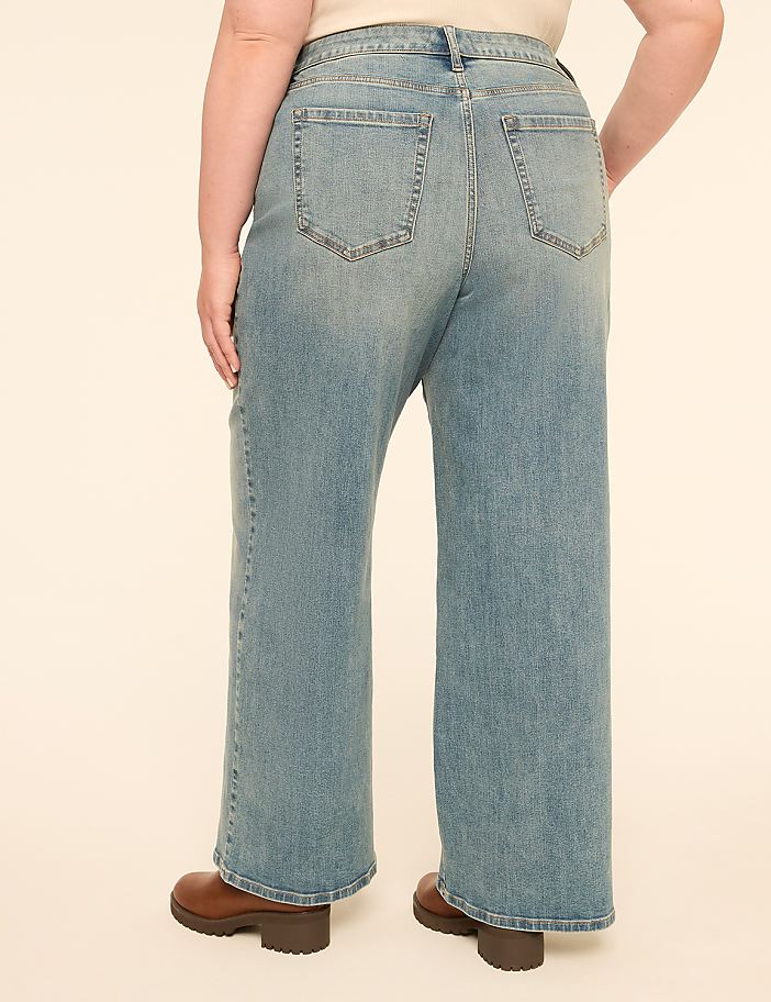 A person wearing light-wash wide-leg jeans and brown boots stands against a plain, light-colored background.