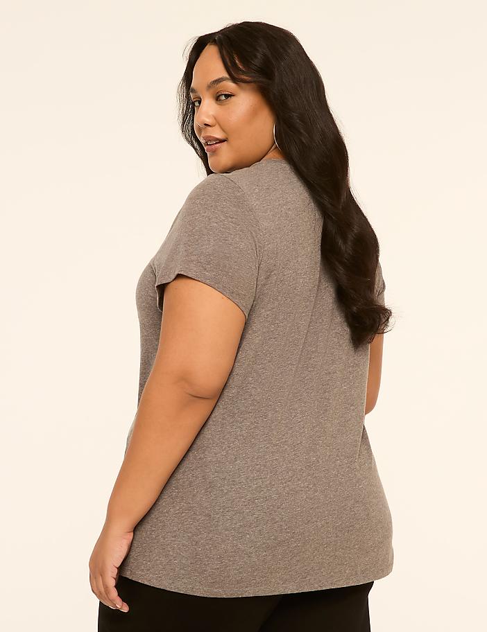 A woman in a gray t-shirt and black pants stands against a plain, light-colored background.