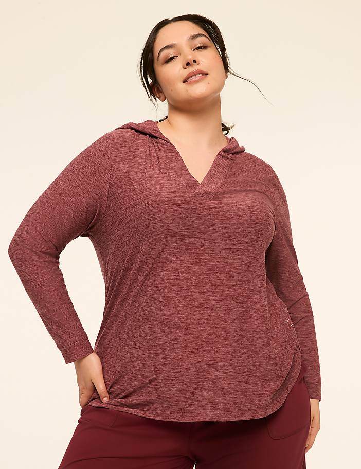 A woman in a maroon hooded shirt and maroon pants stands against a plain, light-colored background.