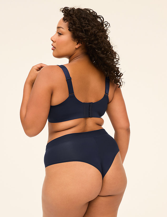 A woman in navy blue lingerie stands against a plain, light-colored background.