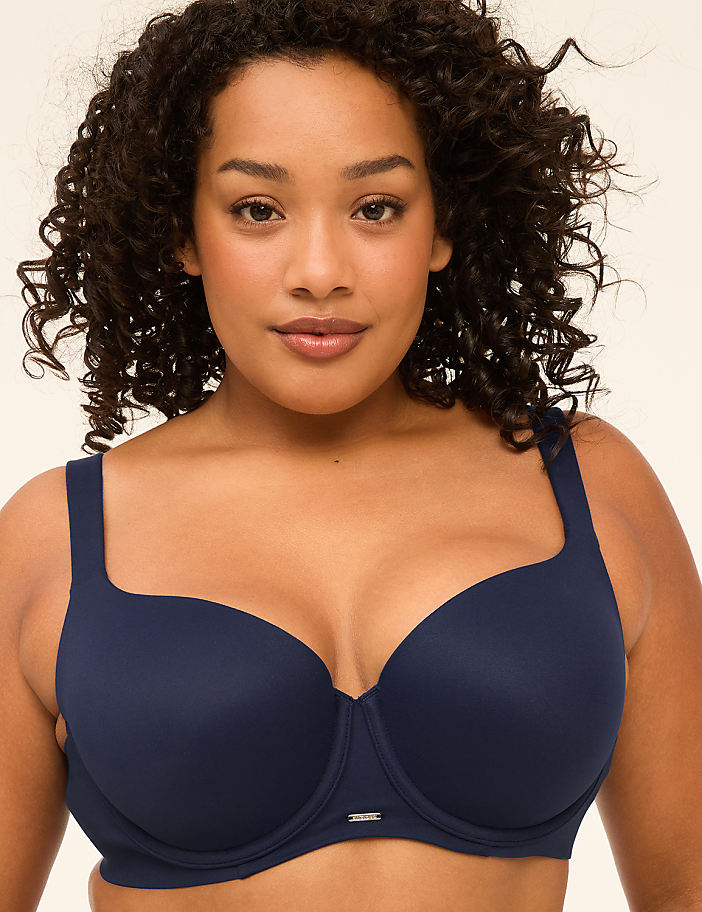A woman with curly dark hair and a navy blue bra is centered against a plain, light background.