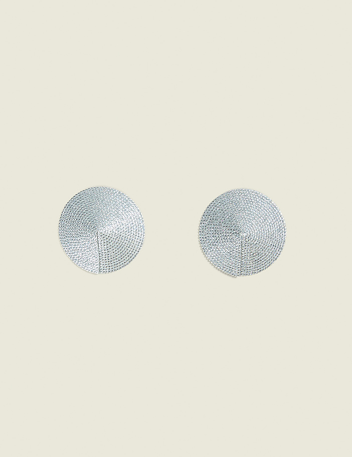 Two circular, textured silver objects are centered on a pale, textured background.