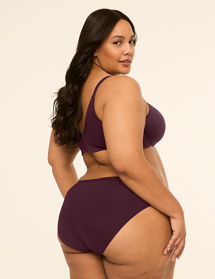 A woman in a plum-colored bra and underwear is shown from the side against a plain, light background.