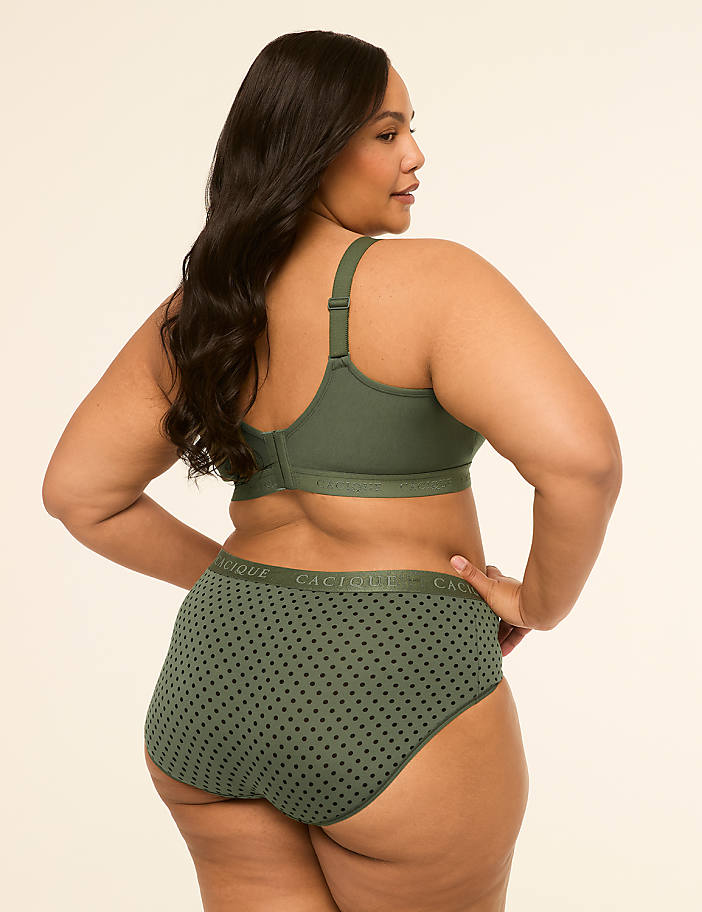 A woman in a green polka dot bra and underwear stands with her back to the camera against a plain, light-colored background.