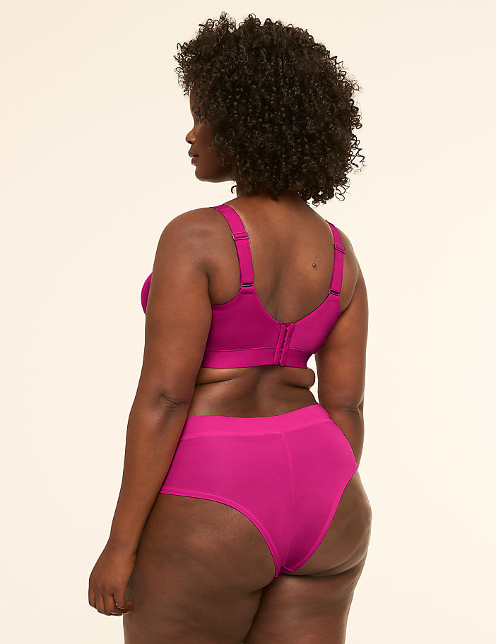 A woman in a magenta bra and underwear stands against a plain cream background.