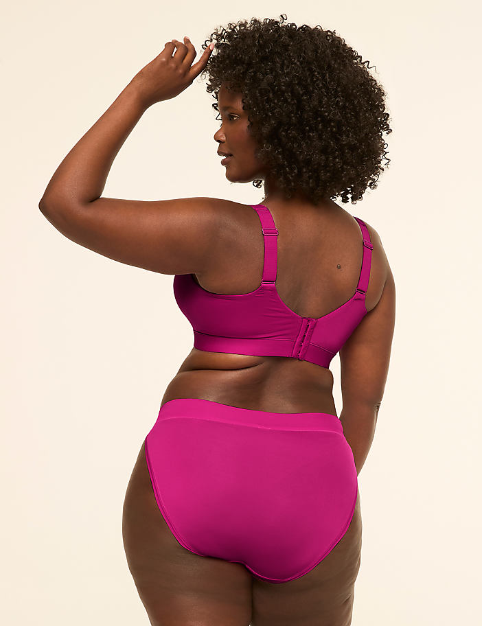 A woman in a magenta bra and underwear poses with her back to the camera against a plain, light background.