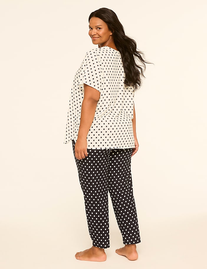 A woman in polka dot pajamas stands against a plain, light-colored background.