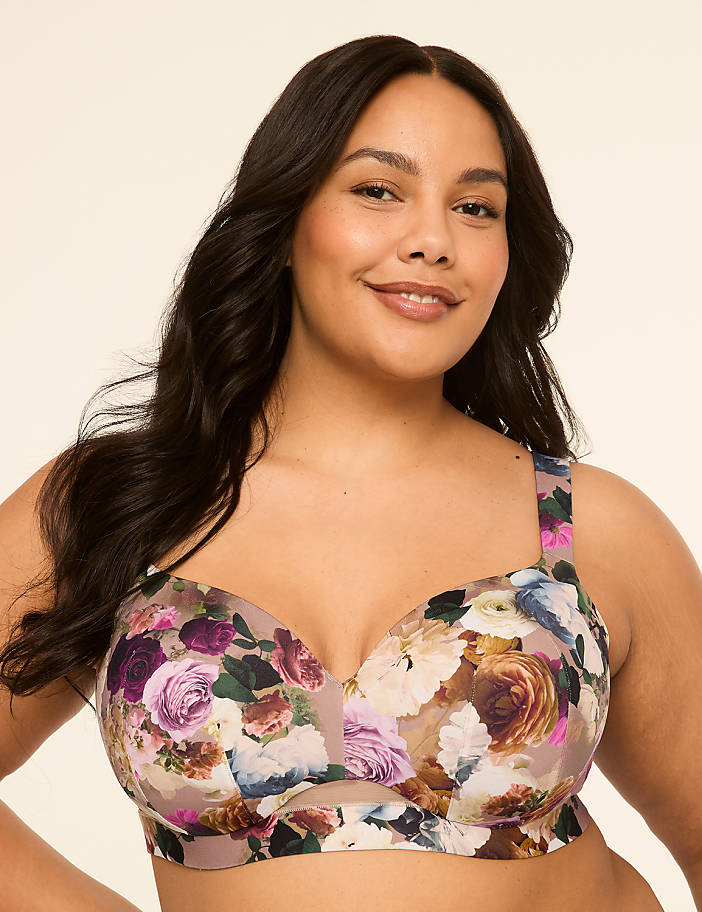 A woman with dark, wavy hair smiles at the camera, wearing a floral-patterned bra against a plain, light-colored background.