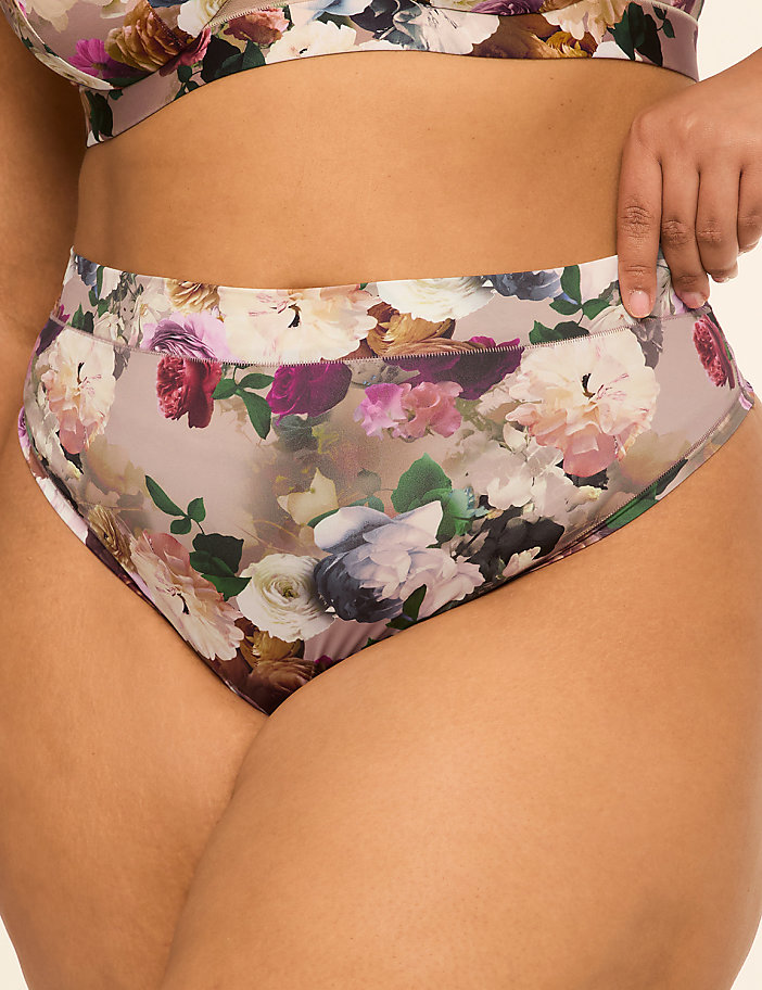 A person wears high-waisted floral underwear in the foreground, with a plain background.