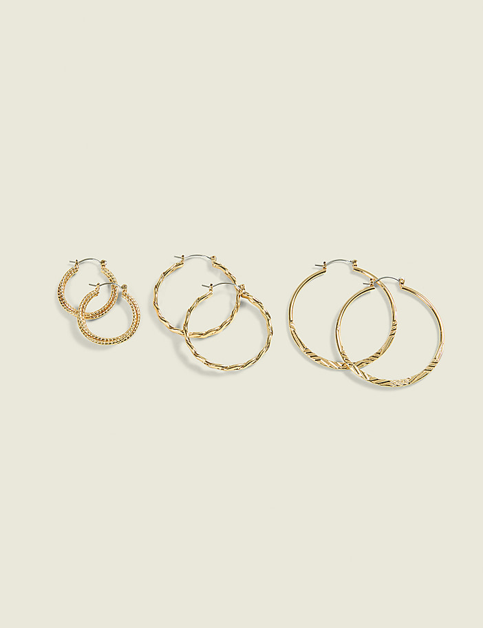 Three pairs of gold hoop earrings, varying in size and texture, are arranged on a plain, light-colored background.