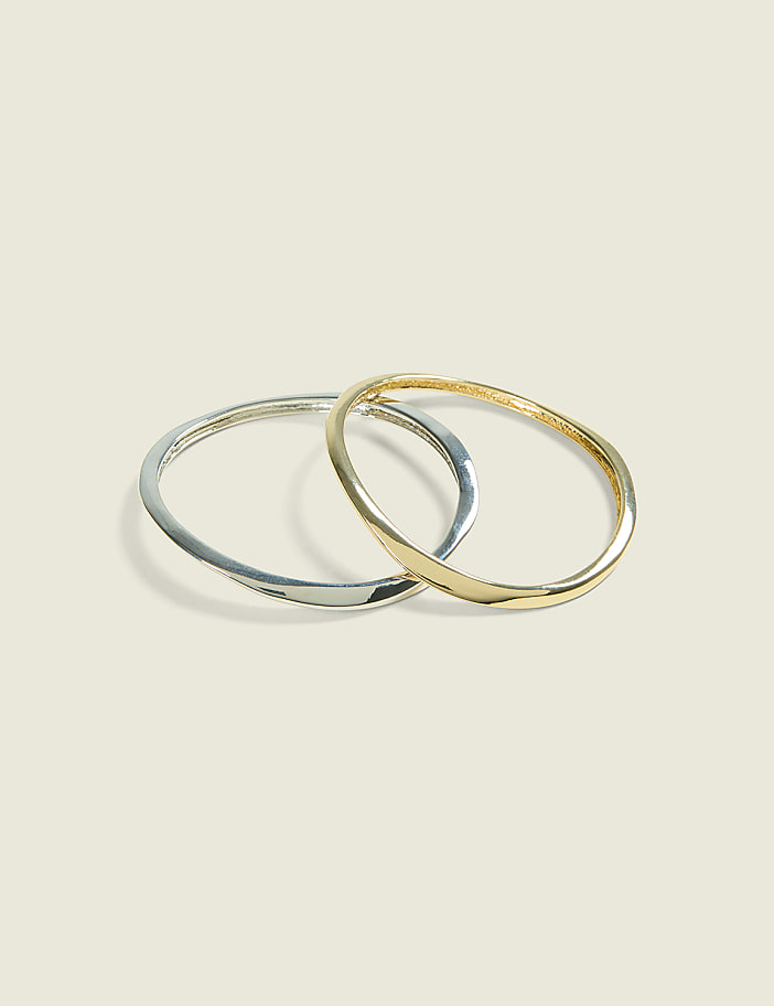 Two intertwined, thin bangles, one silver and one gold, rest on a pale, textured background.