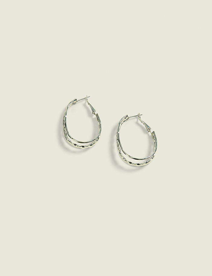 A pair of silver oval hoop earrings with textured detailing rests on a pale green background.